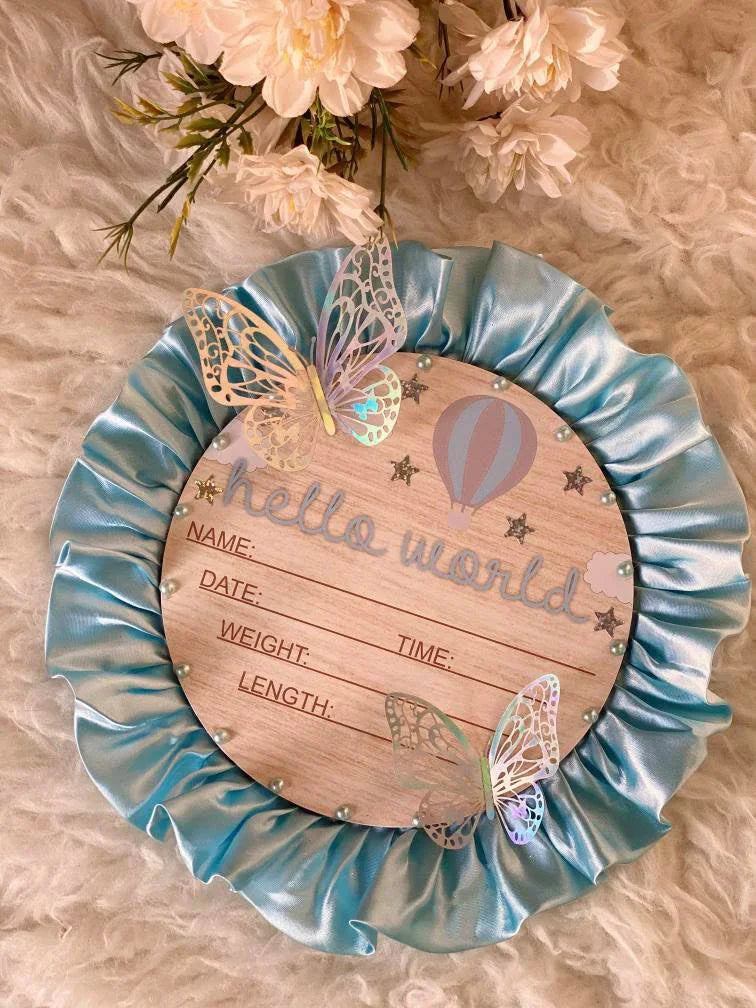 Hello World baby announcement plaque with butterflies, hot air balloon, and satin ruffle border on fluffy background