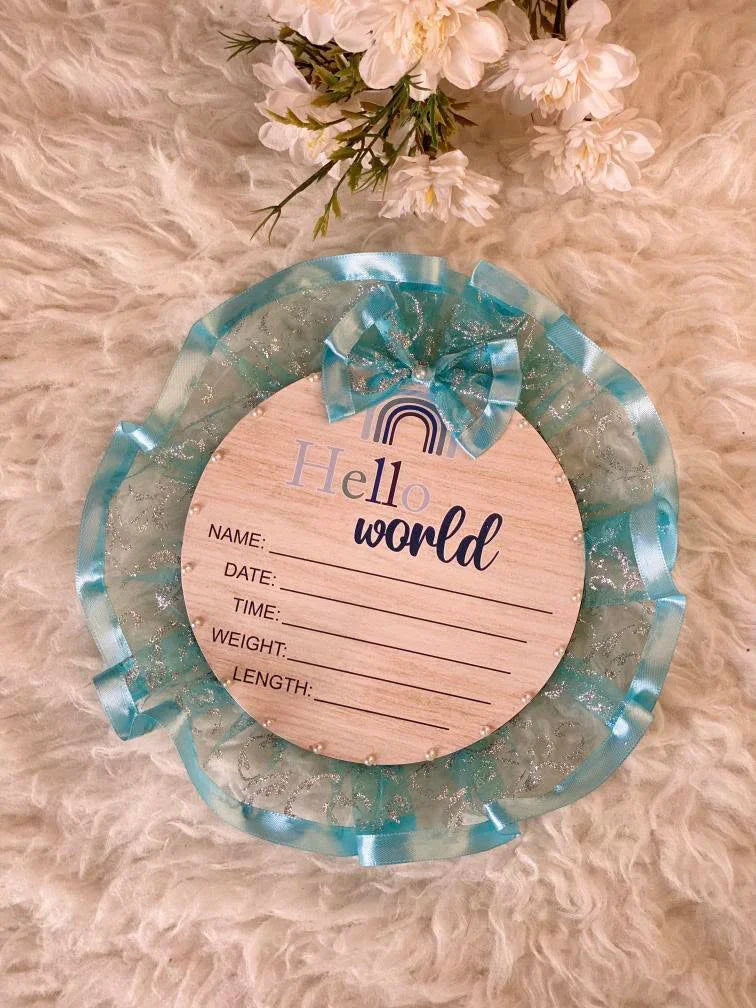 Hello World baby announcement plaque with blue ribbon on fluffy background