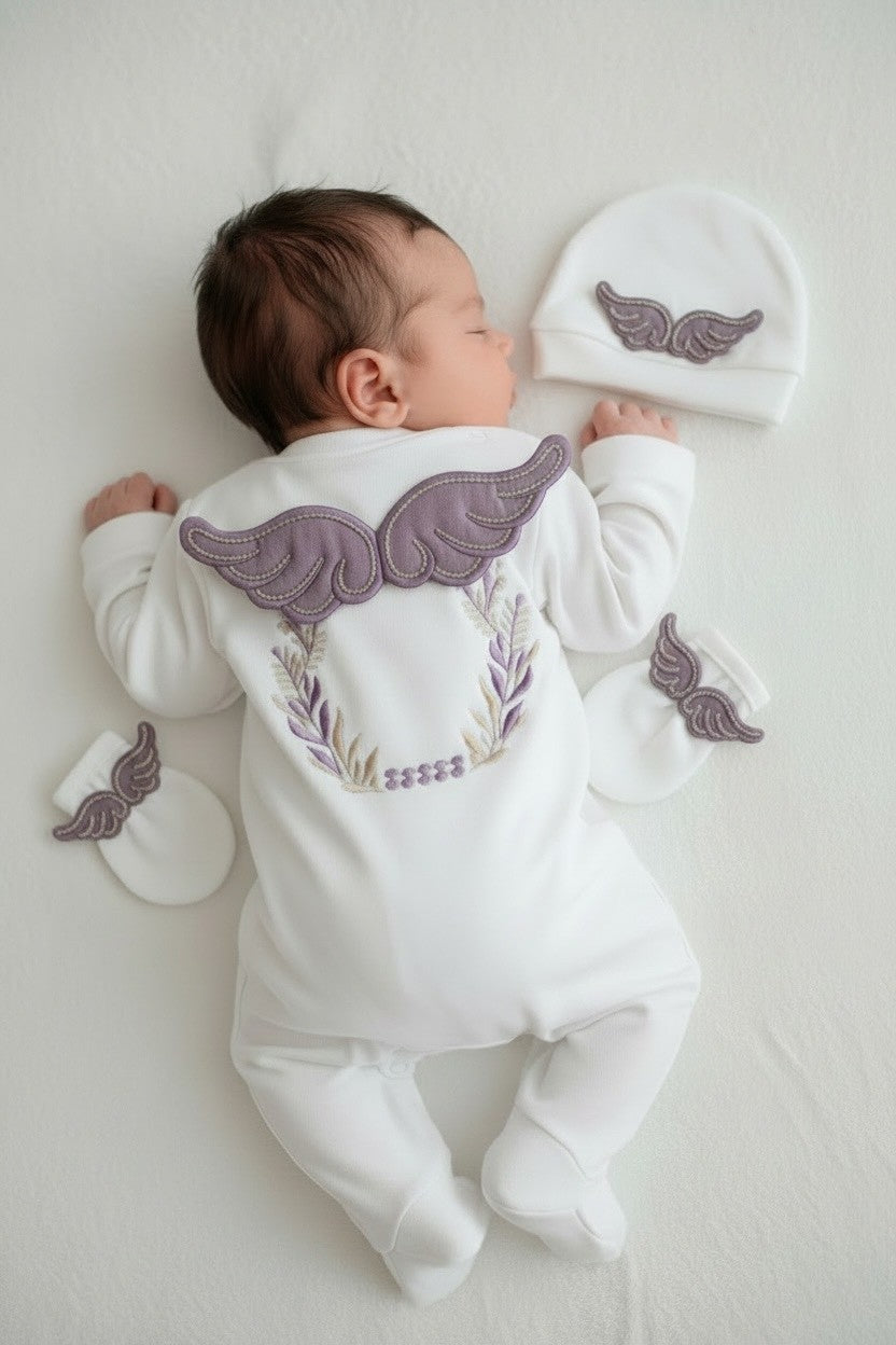 Newborn baby in white organic cotton romper with purple angel wings, matching hat and mittens set
