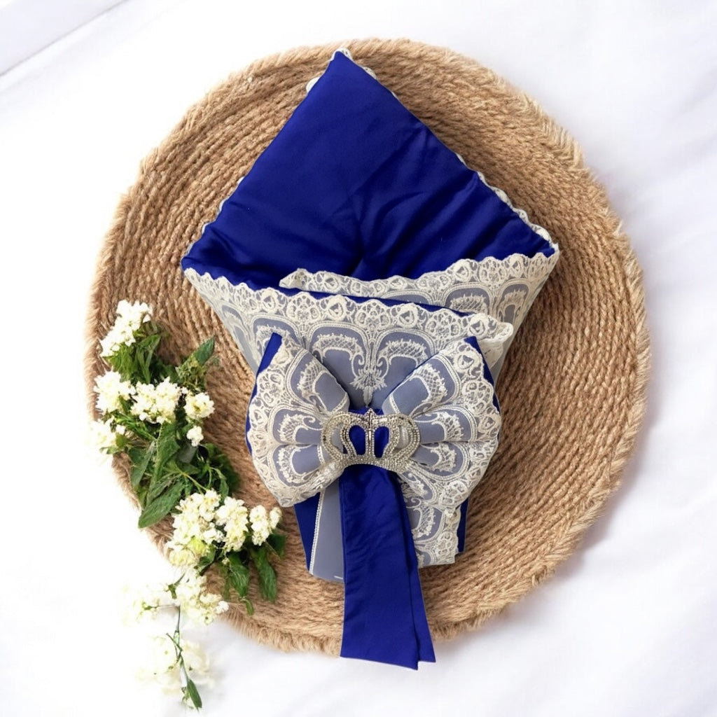 Royal blue baby romper with lace trim and bow, styled on woven mat with white flowers