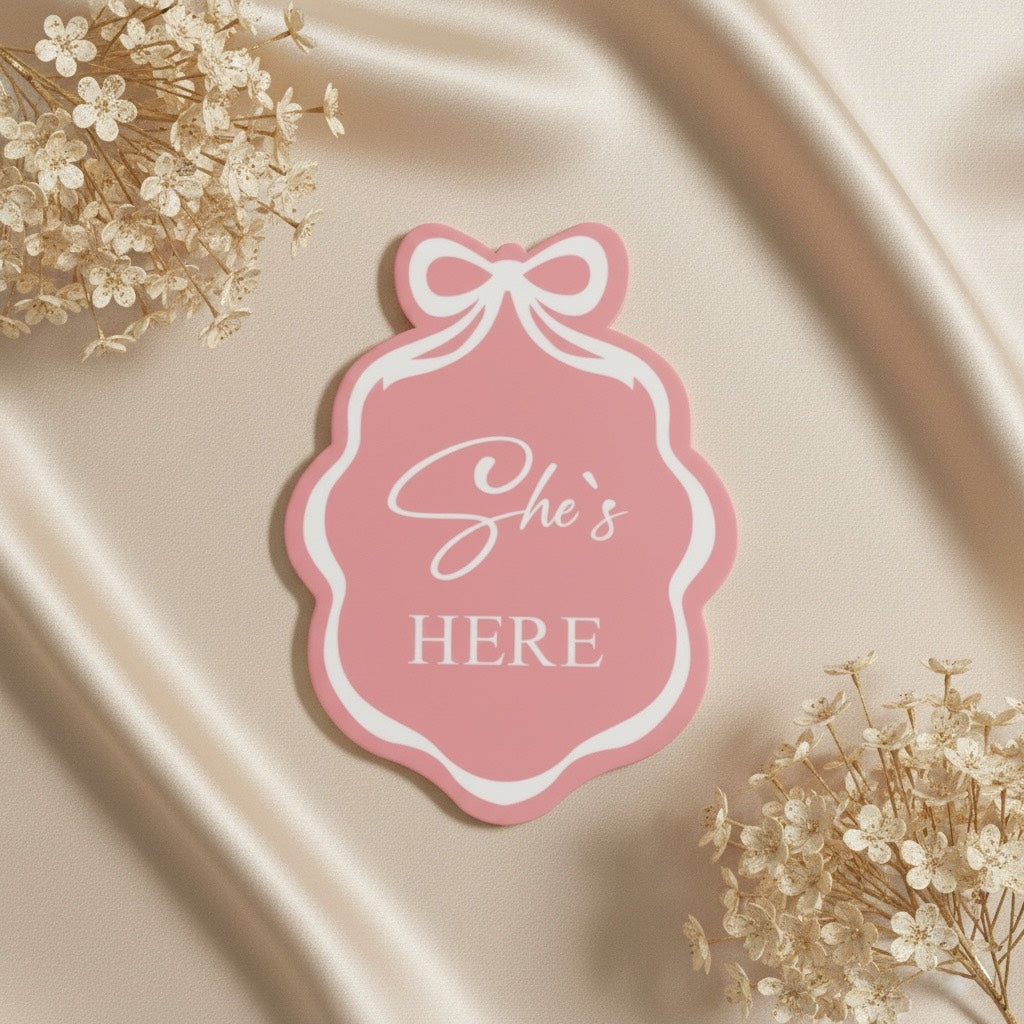 Pink 'She's Here' baby announcement tag with bow, on satin with dried flowers, for newborn baby gifts